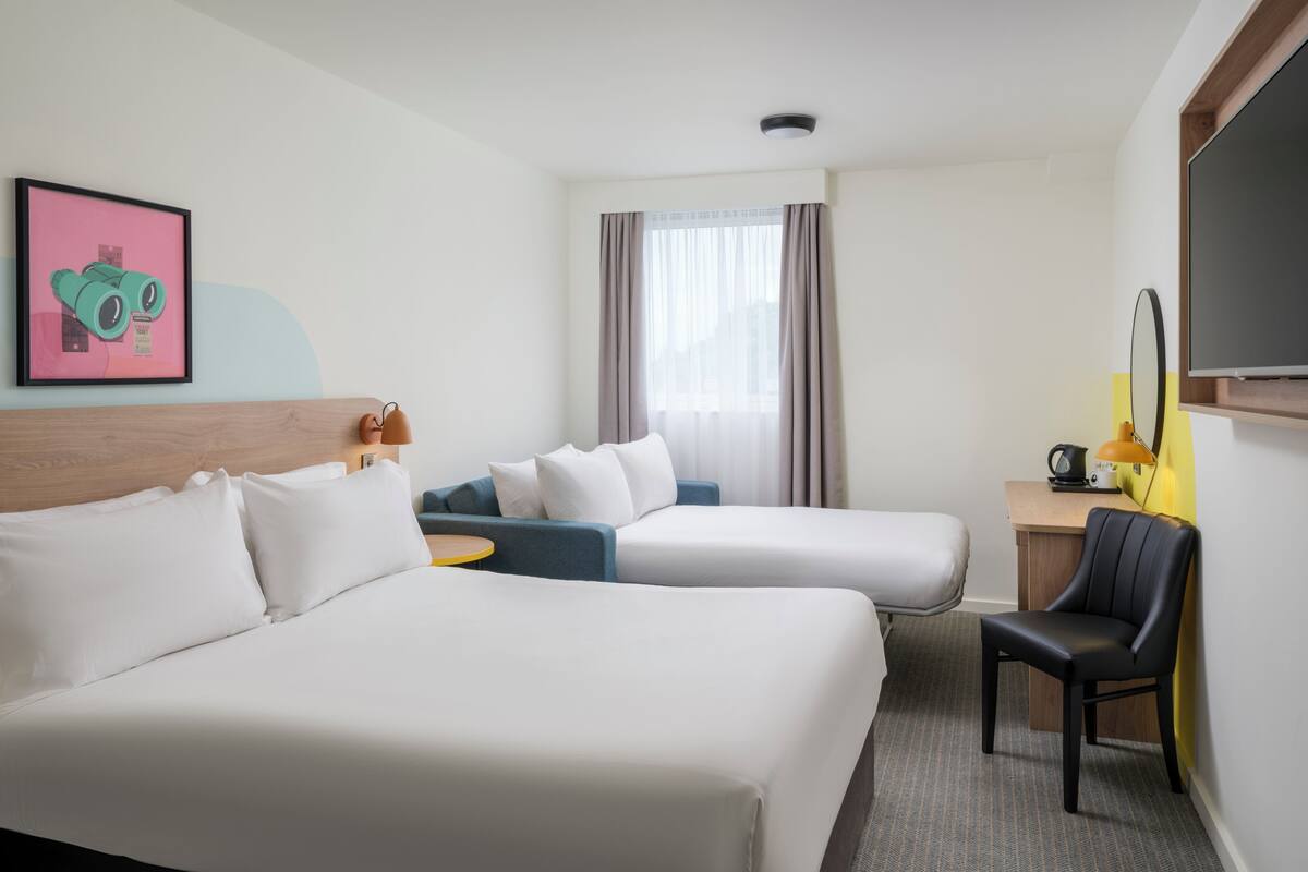 A hotel room with two beds, a desk with a chair, a television, and a window with curtains.