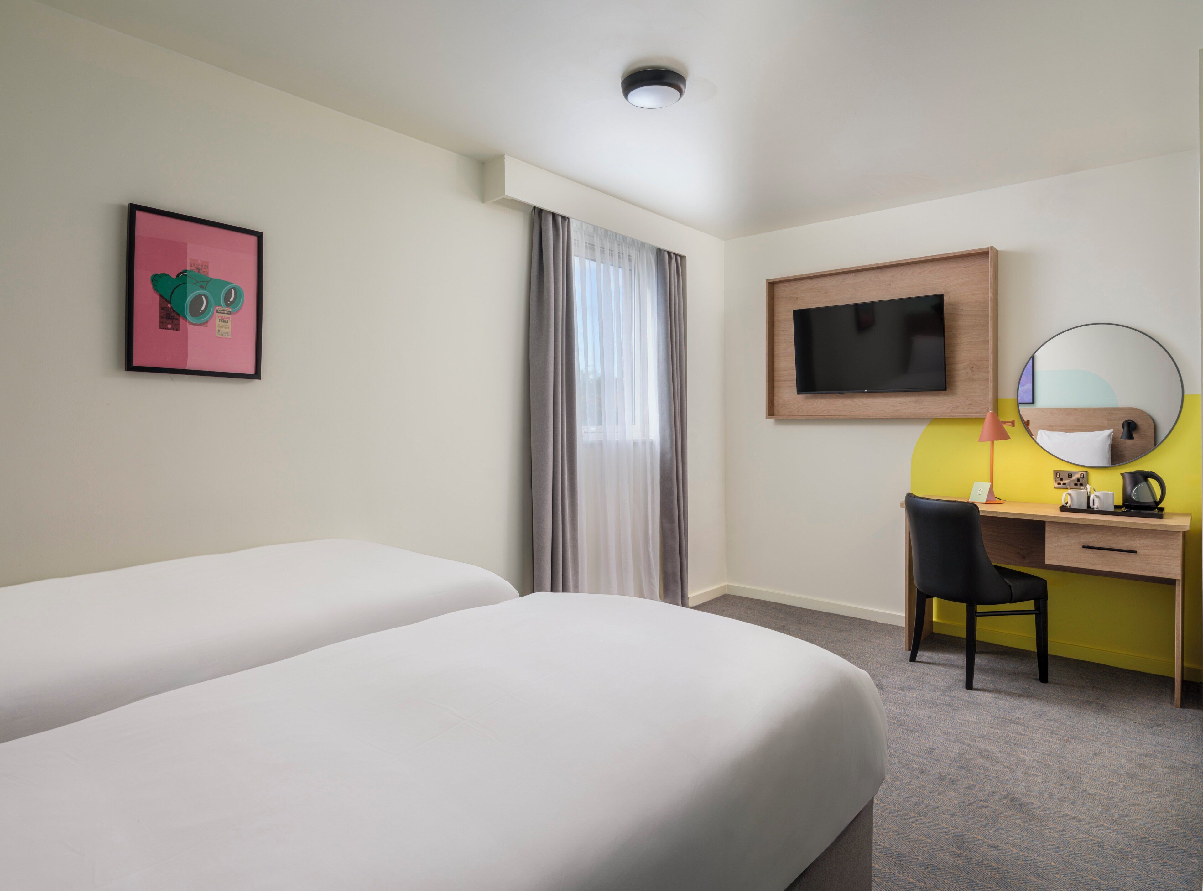 A hotel room with two beds, a desk with a chair, a television, a mirror, and a picture on the wall.