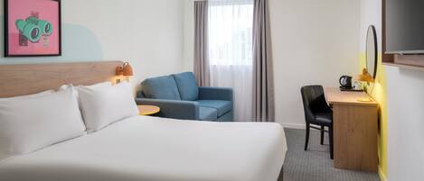 A hotel room with a large bed, a desk with a chair, a small table, a TV, and a window with curtains.