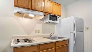 A kitchen with wooden cabinets, a white countertop, a stove, a microwave, a sink, and a refrigerator. - Extended Stay America Select Suites - Fort Walton Beach (Fort Walton Beach)