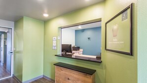 A reception area with a wooden counter, a computer, and a framed welcome sign. - Extended Stay America Select Suites - Fort Walton Beach (Fort Walton Beach)
