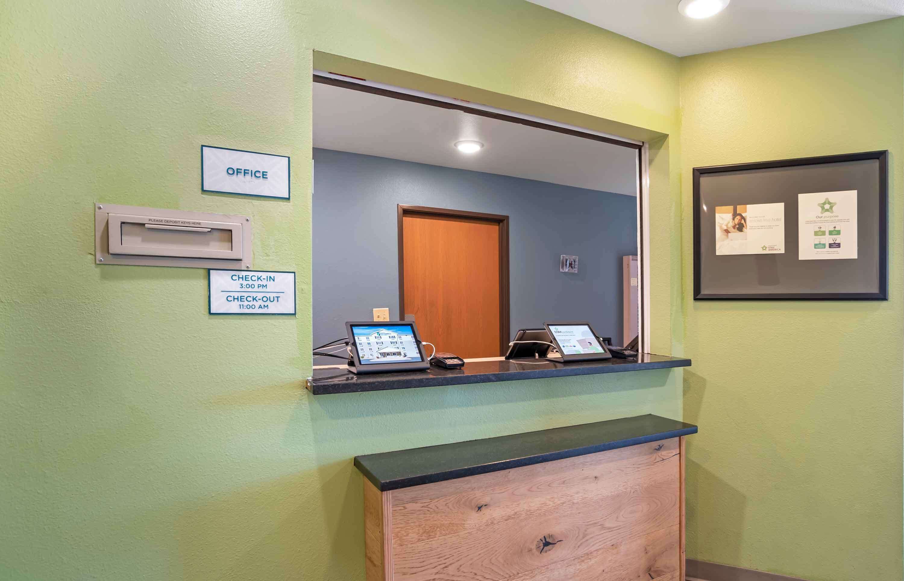 A reception desk with a check-in/out sign, a mirror, and a framed certificate on the wall.