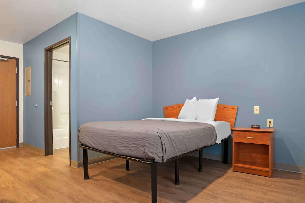 A bedroom with a bed, a nightstand, a wooden floor, and a door.