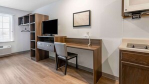 A modern hotel room with a wooden desk, a television, a chair, a wardrobe, and a bathroom vanity. - Extended Stay America Select Suites - Fort Walton Beach (Fort Walton Beach)