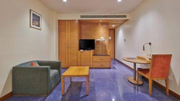 A compact living space with a sofa, a small table, a TV, a desk with a chair, and a wardrobe.