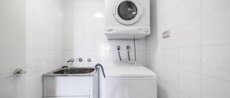 Un espace buanderie compact comprenant un lave-linge, un sèche-linge et un évier.