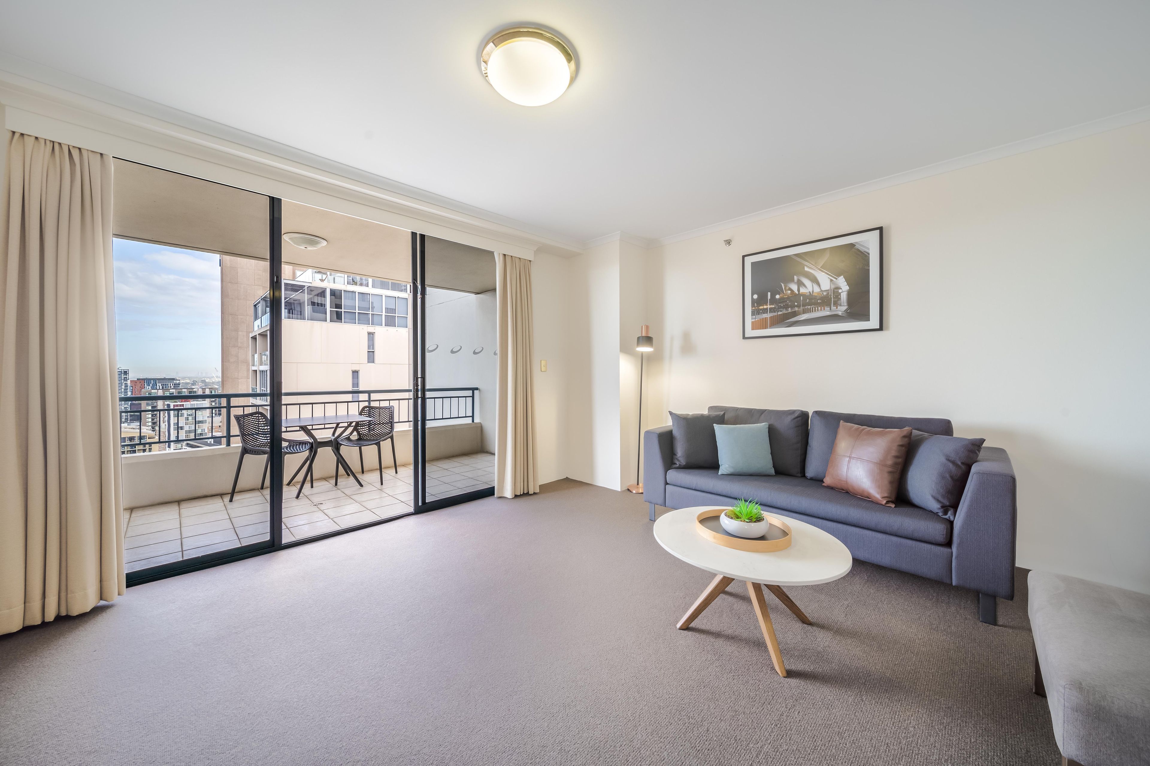 A modern living room with a grey sofa, a small round coffee table, and a balcony with a view of the city.