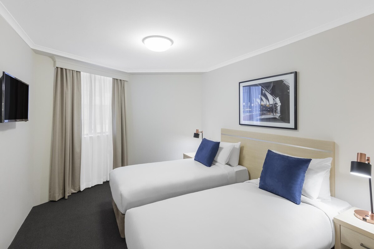 Habitación de hotel con dos camas, un televisor de pantalla plana, un cuadro en la pared y una ventana con cortinas.