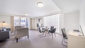 Habitación de hotel con sofá, mesa de comedor con sillas, escritorio con lámpara y ventanas amplias.