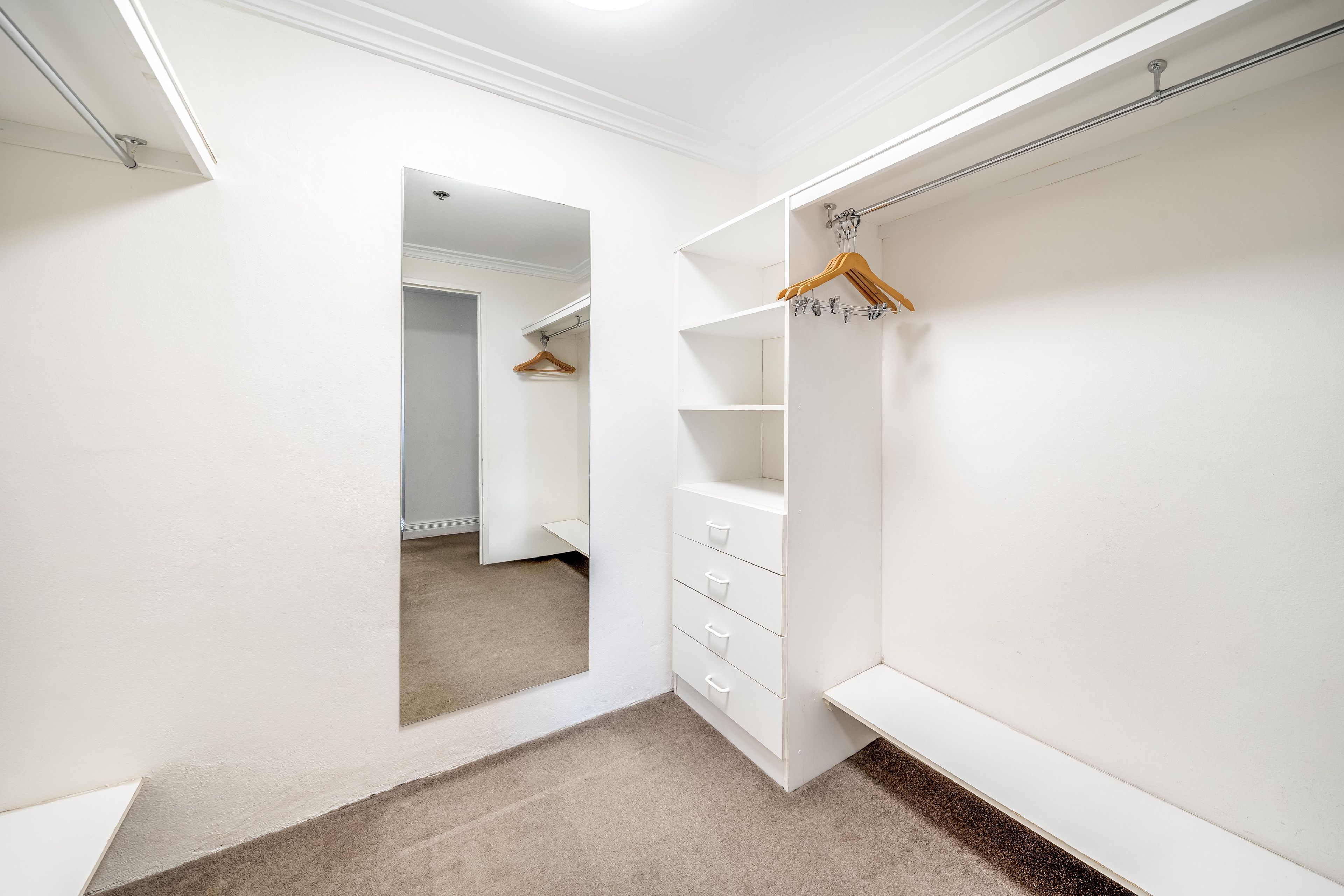 Ein begehbarer Kleiderschrank mit Kleiderstange, offenen Regalen und einer spiegelnden Schiebetür.