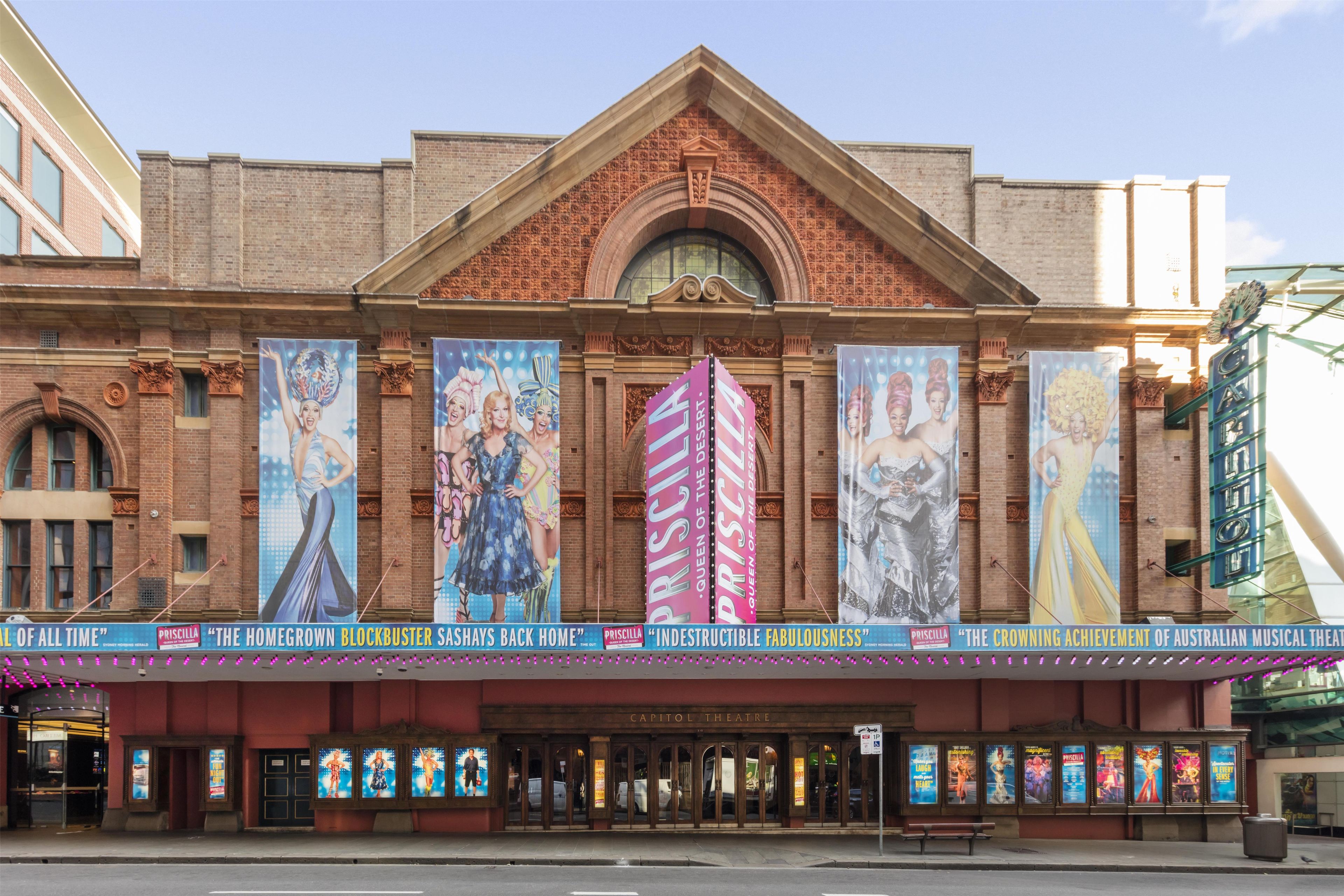 A theater with a classic brick facade, large posters advertising shows, and a marquee with show titles.