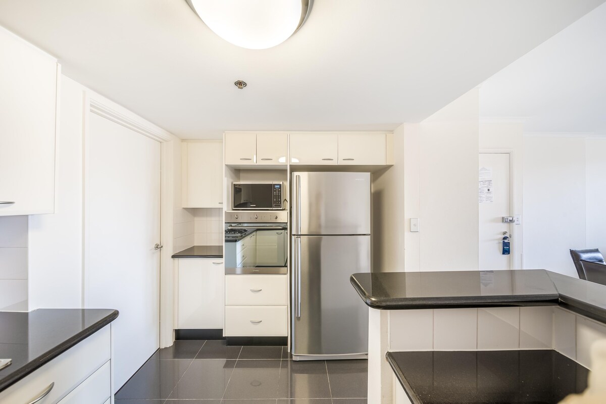 Una cocina moderna con armarios blancos, un refrigerador de acero inoxidable, un microondas y un horno.