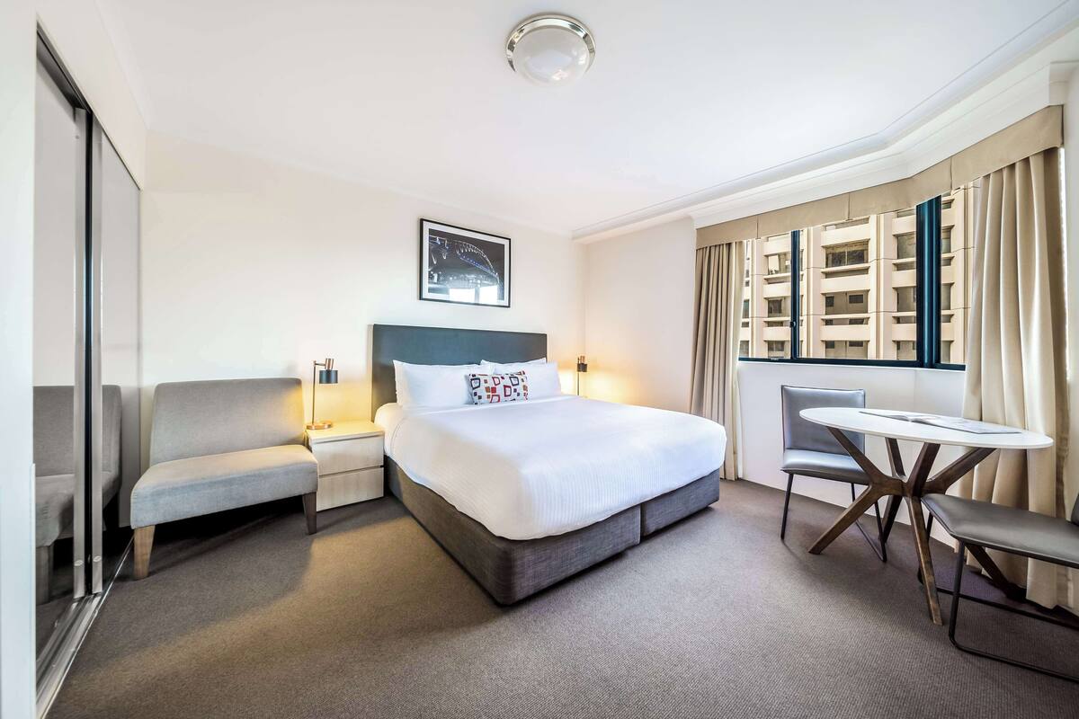 A hotel room with a large bed, a sofa, a small table, and a window with curtains.