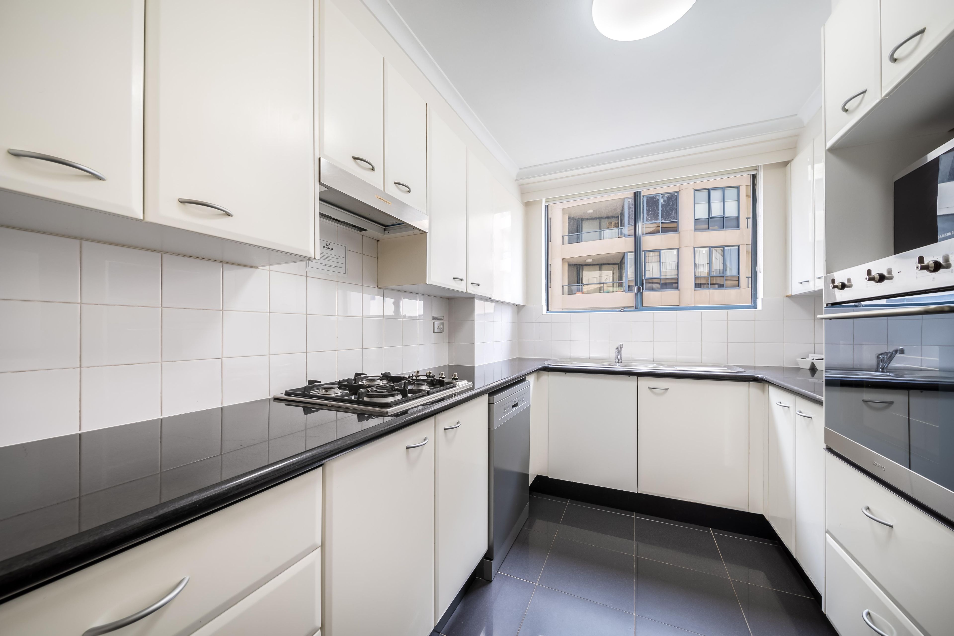 A modern kitchen with white cabinets, a black countertop, and a built-in oven.