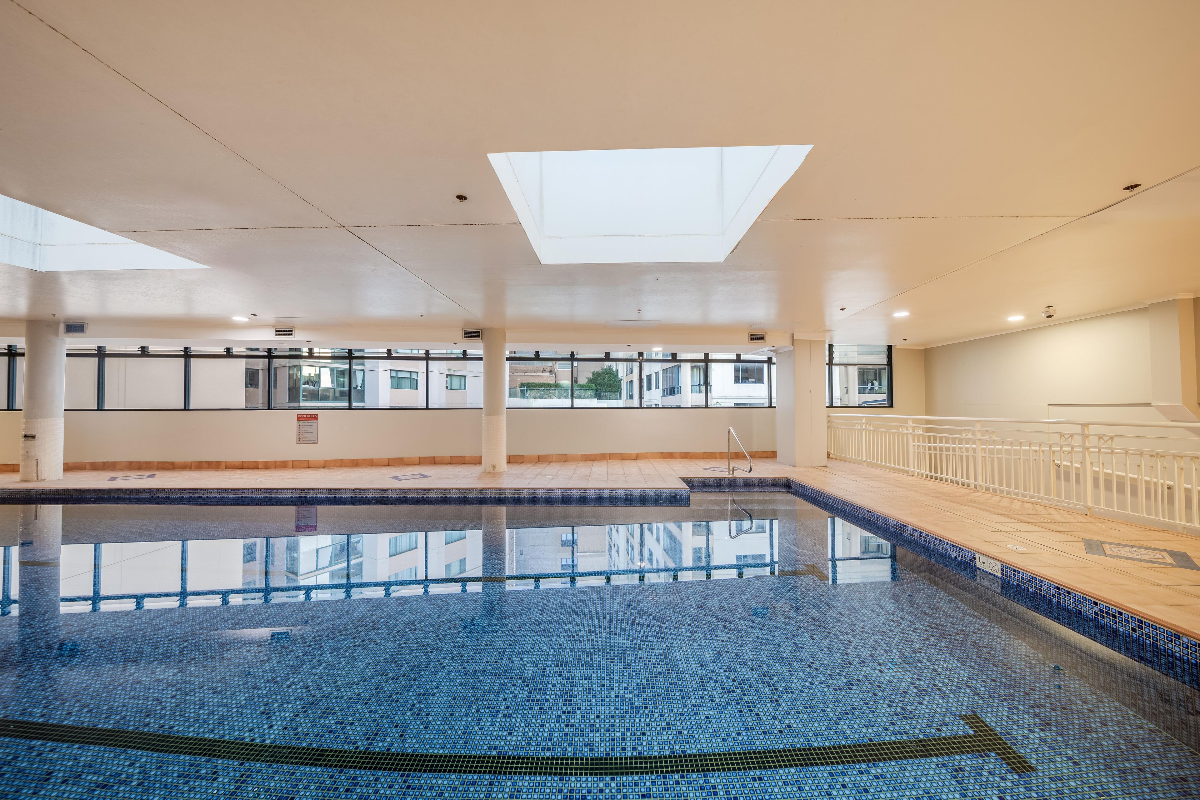 An indoor swimming pool with clear glass walls, a tiled floor, and a skylight above.