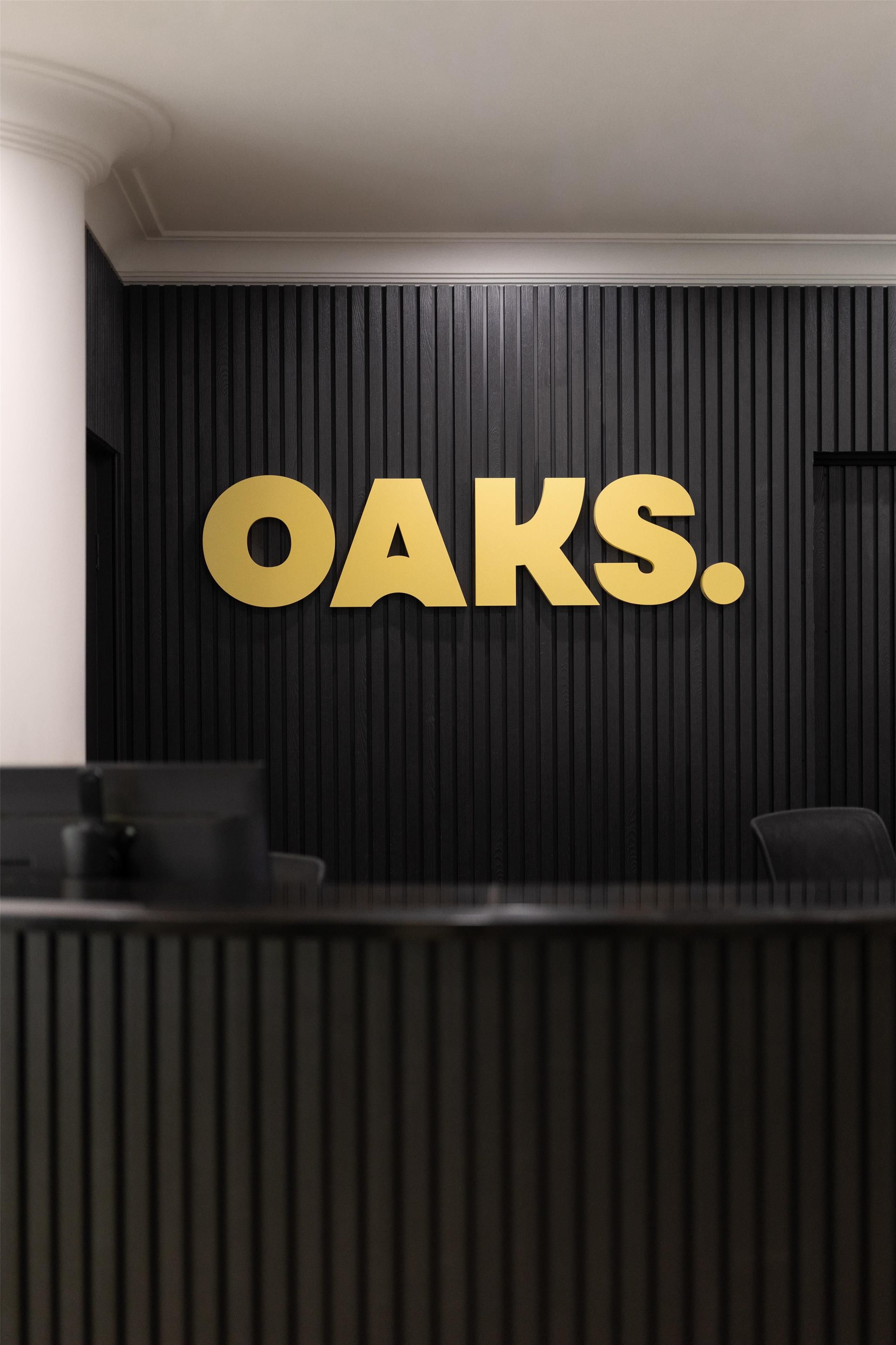Un comptoir d’accueil avec un mur en panneaux noirs et le mot « OAKS » inscrit en lettres dorées.