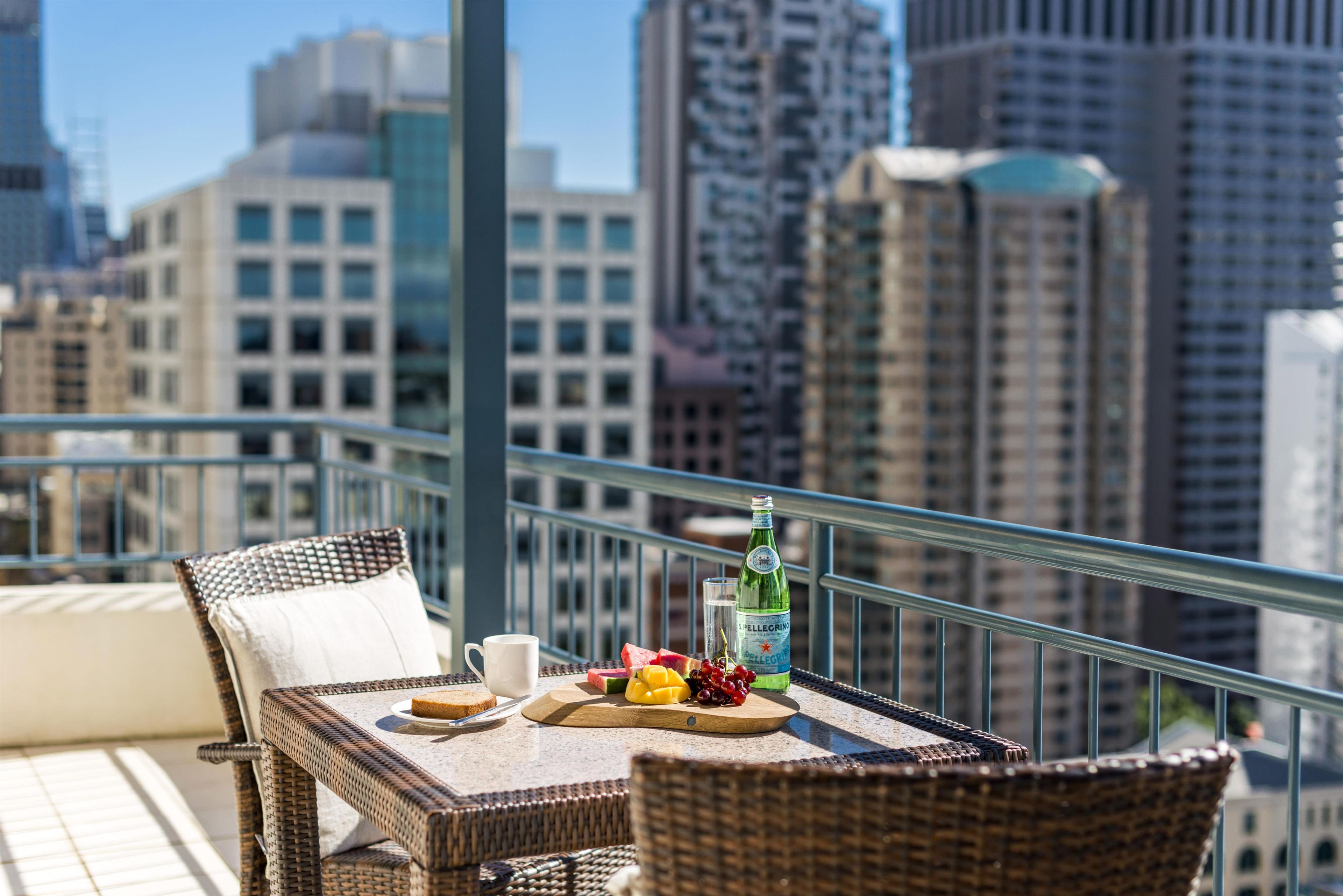 A balcony with wicker furniture, a bottle of Pellegrino water, and a fruit platter.