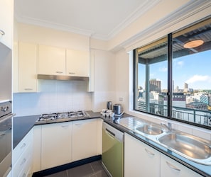 Cocina moderna con armarios blancos, estufa a gas, lavavajillas y un amplio ventanal con vistas a la ciudad.