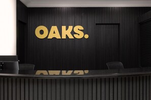 A reception desk with a dark wood panel wall and large gold letters spelling 'OAKS.' - Oaks Sydney Castlereagh Suites (Haymarket)
