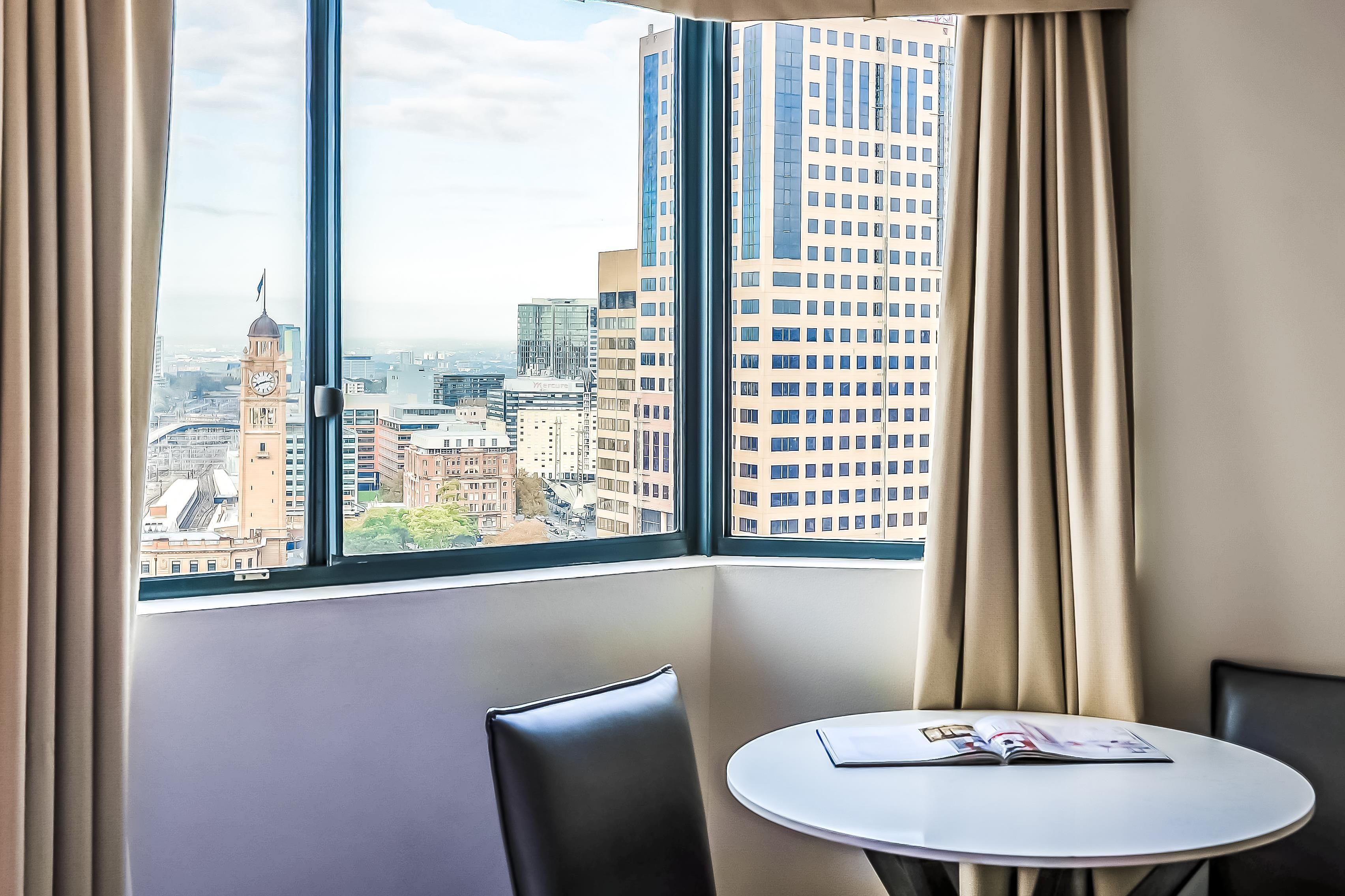 A hotel room with a large window offering a city view, a small round table, and two chairs.