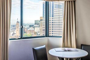 A hotel room with a large window offering a city view, a small round table, and two chairs. - Oaks Sydney Castlereagh Suites (Haymarket)