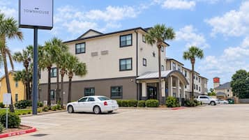 A multi-story hotel with a sign reading 'OYO TOWNHOUSE' and a parking lot with cars.