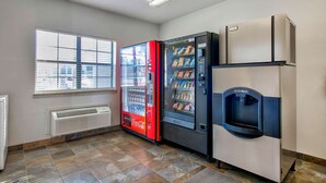 Ein Zimmer mit Fenster, einem roten Coca-Cola-Kühlschrank, einem Eisbereiter und einer weißen Klimaanlage.