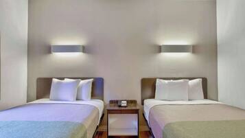 Habitación de hotel con dos camas, una mesita de noche con teléfono e iluminación en la pared.