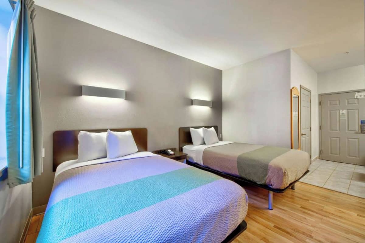 Habitación de hotel con dos camas, piso de madera y una puerta.