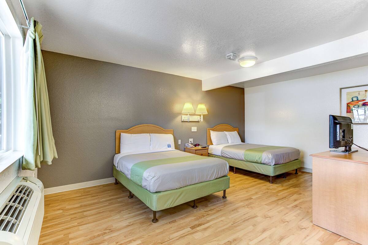 A hotel room with two beds, a desk, a heater, and a window with curtains.