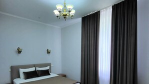 A hotel room with a large bed, a chandelier, two wall sconces, and a window with curtains. - Vila Verde (Chisinau)