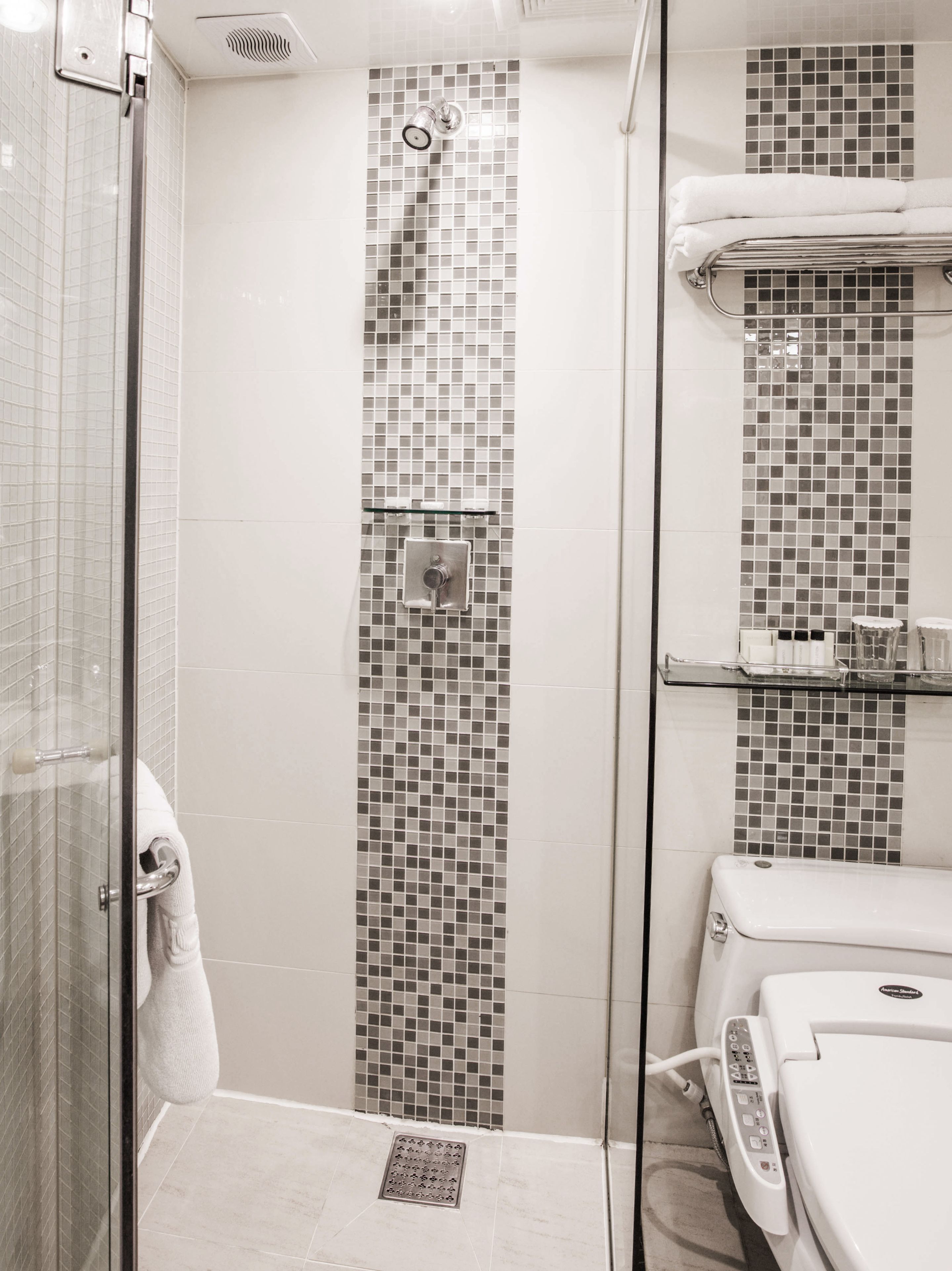 A bathroom with a glass shower enclosure, a tiled shower wall, a toilet with a control panel, and a towel rack.