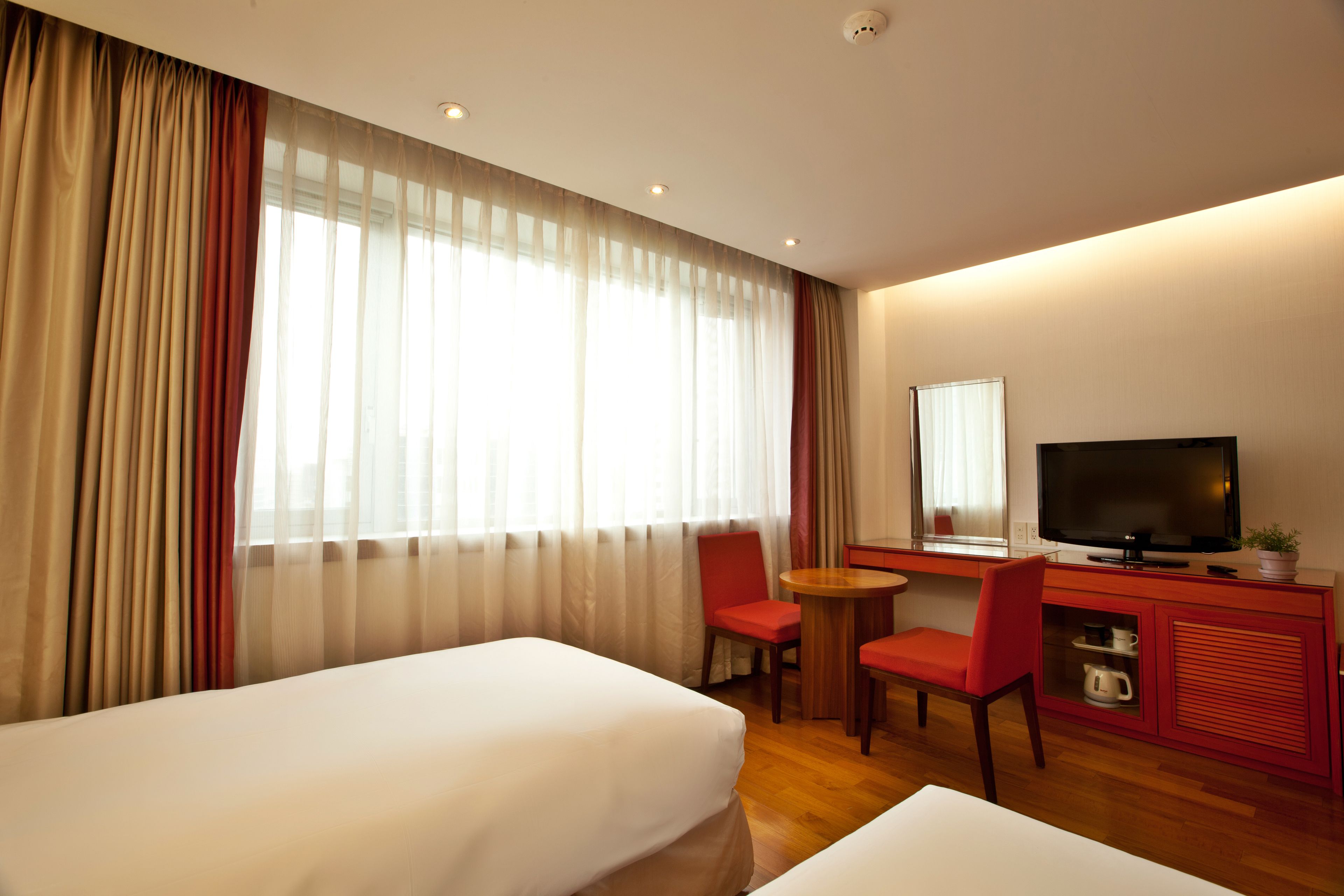 Ein Hotelzimmer mit zwei Betten, einem Schreibtisch mit Fernseher, einem Sessel und einem kleinen Tisch.