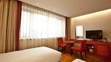 Ein Hotelzimmer mit zwei Betten, einem Schreibtisch mit Fernseher, einem Sessel und einem kleinen Tisch.