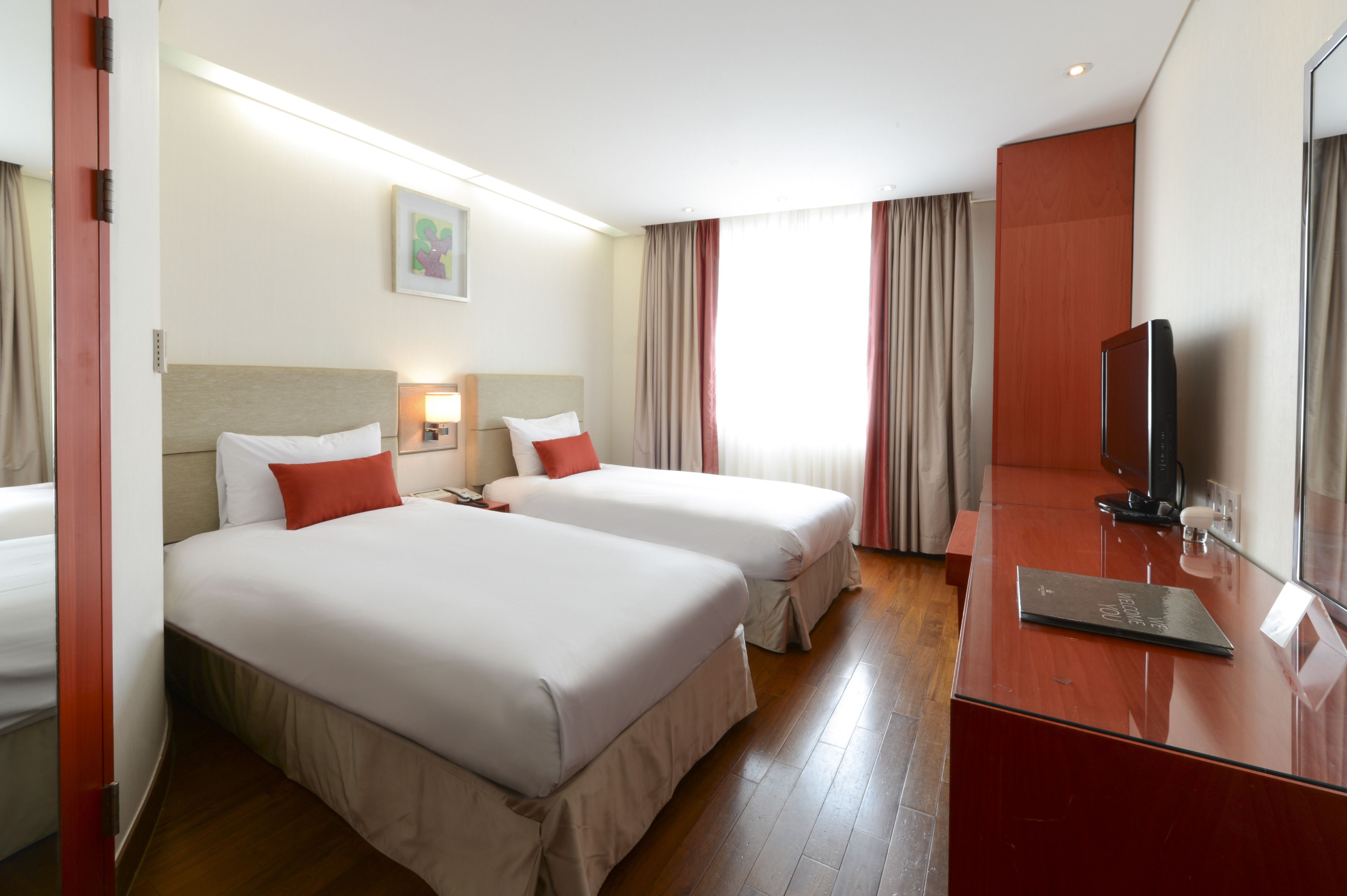 Une chambre d’hôtel avec deux lits, un bureau, une télévision et une fenêtre avec des rideaux.