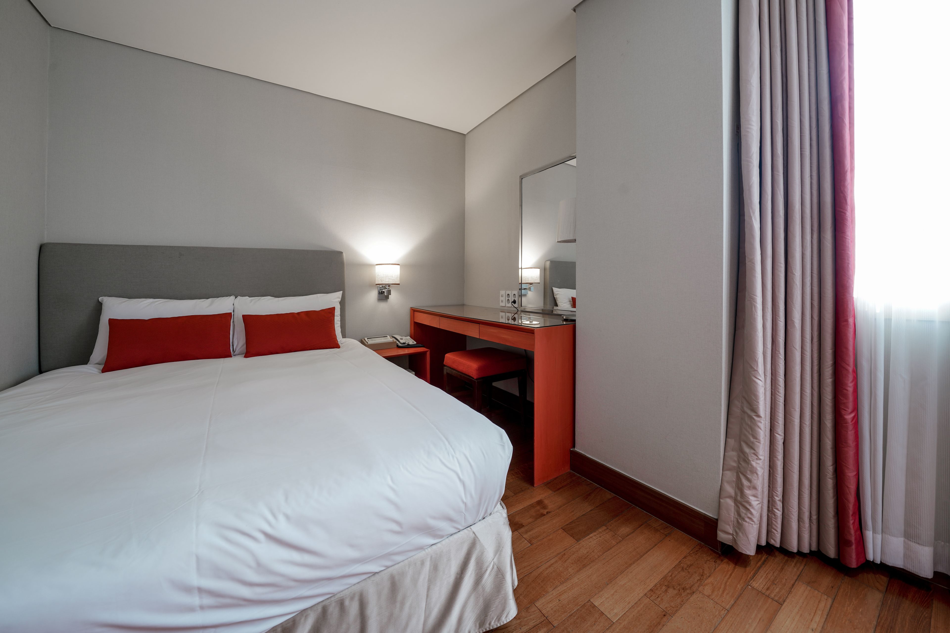 A hotel room with a large bed, a desk, and a mirror.