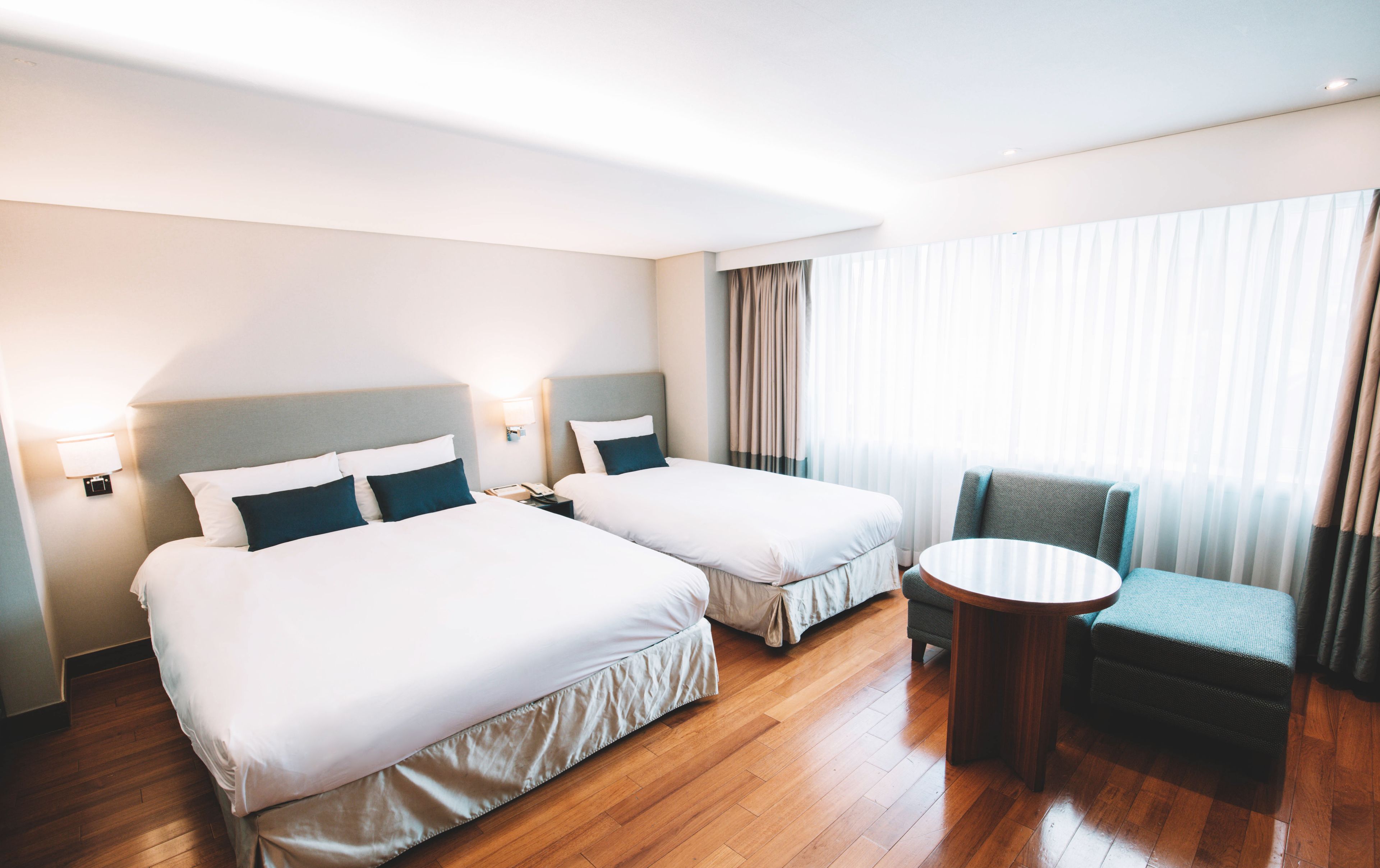 Habitación de hotel con dos camas, una mesita redonda y una silla.