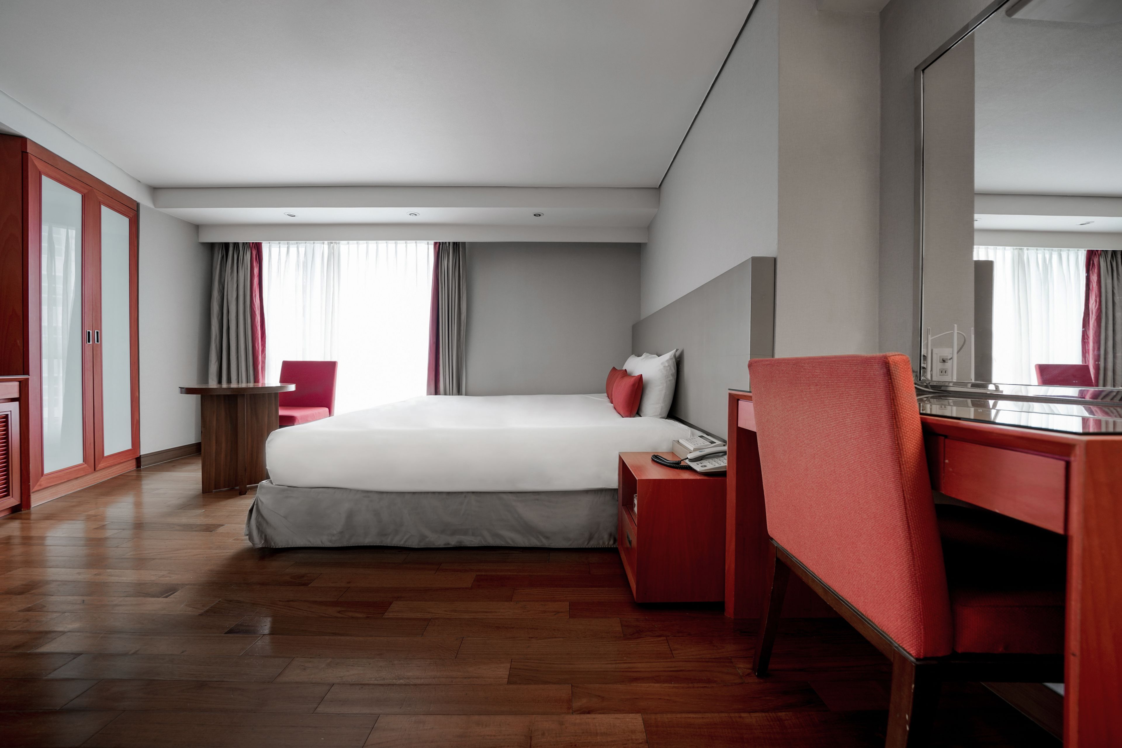 Una habitación de hotel con una cama grande, un escritorio con silla, un armario y un espejo.