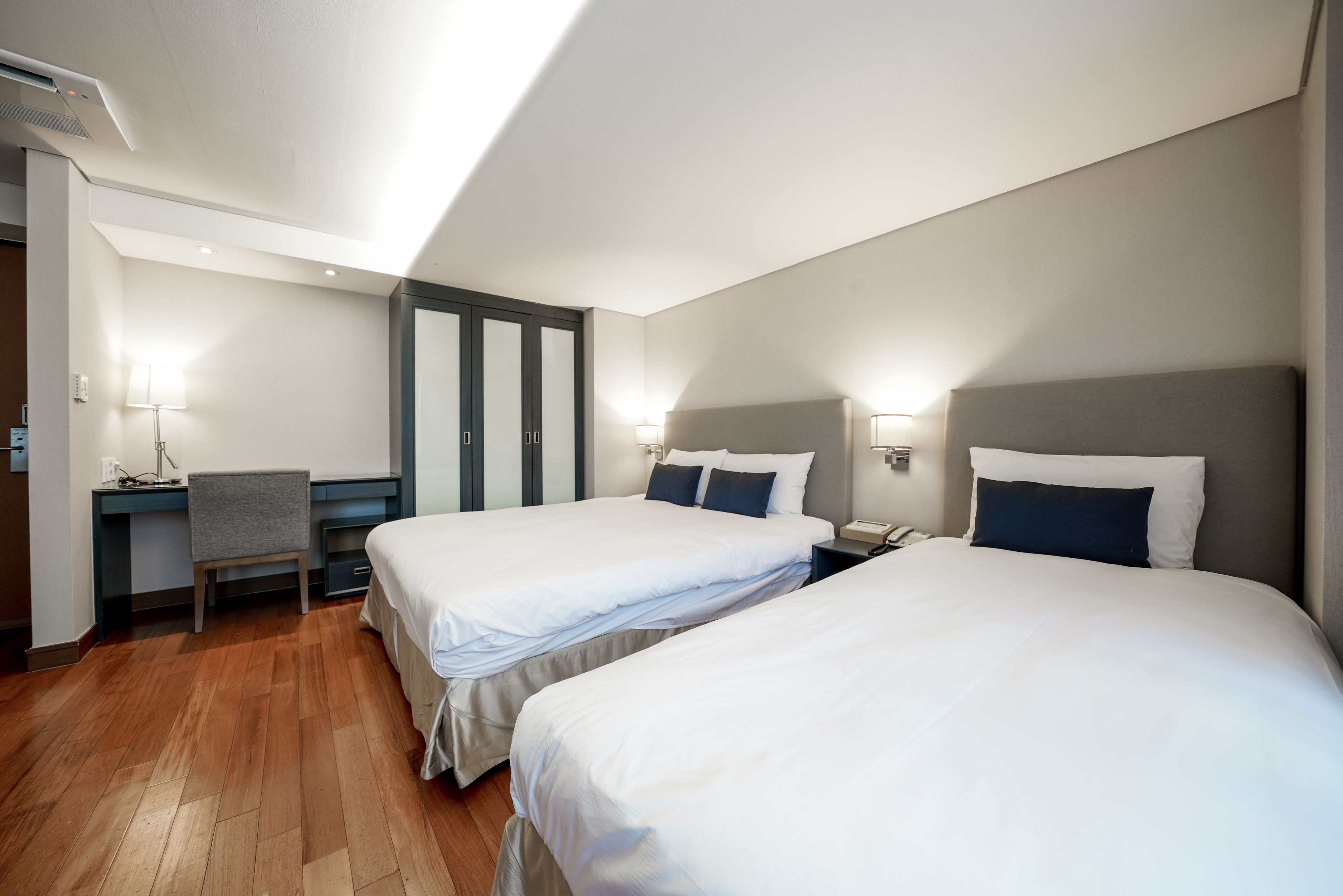 A hotel room with two beds, a desk, and a chair.