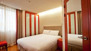 A hotel room with a large bed, a bedside table, a bench, and a wardrobe with a mirror.