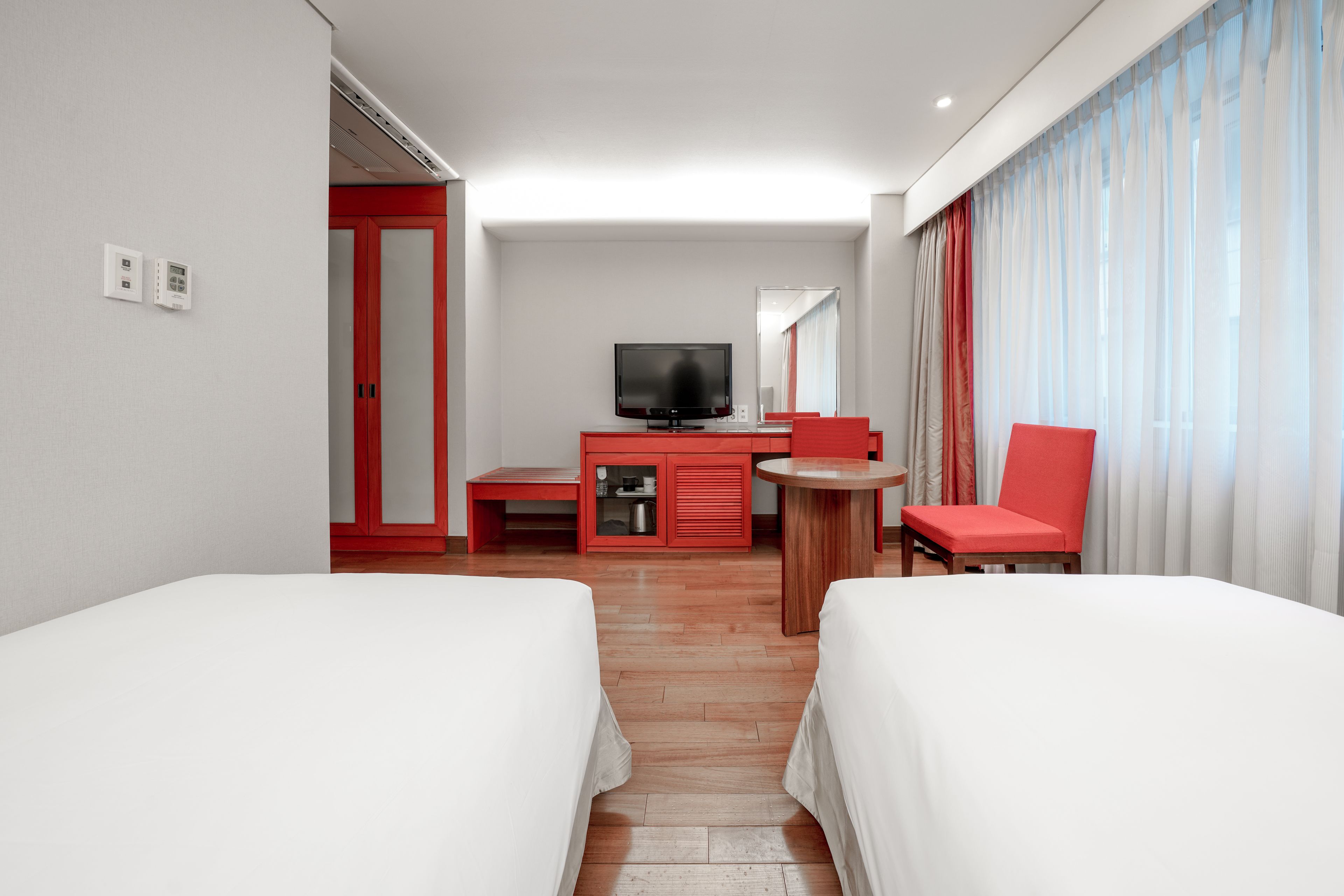 A hotel room with two beds, a TV, a desk with a chair, and a window with curtains.