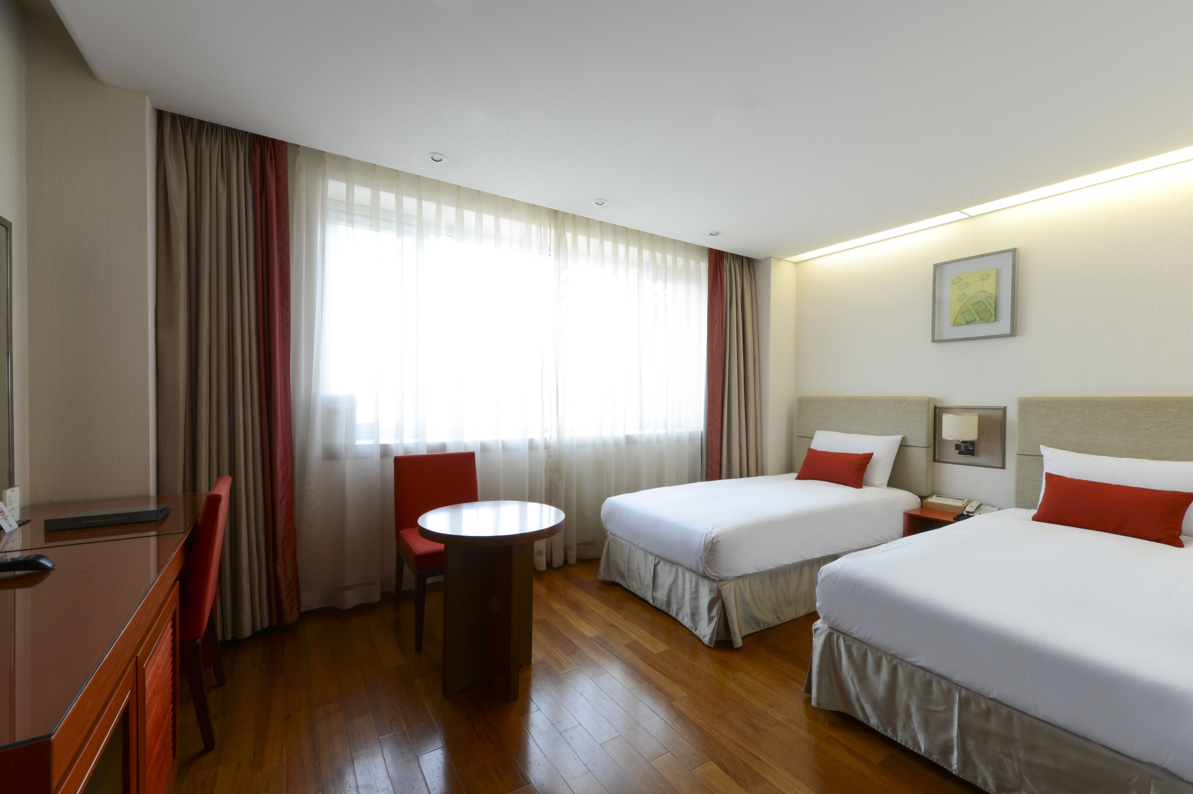 Ein Hotelzimmer mit zwei Betten, einem Schreibtisch, einem Stuhl und einem fenster mit Vorhängen.