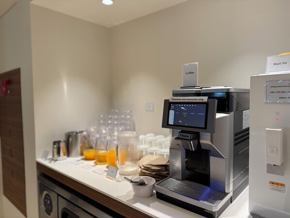 Una cafetera con pantalla digital, una estación de café con tazas y jarra, y un letrero que indica 'Solo espresso y americano'.