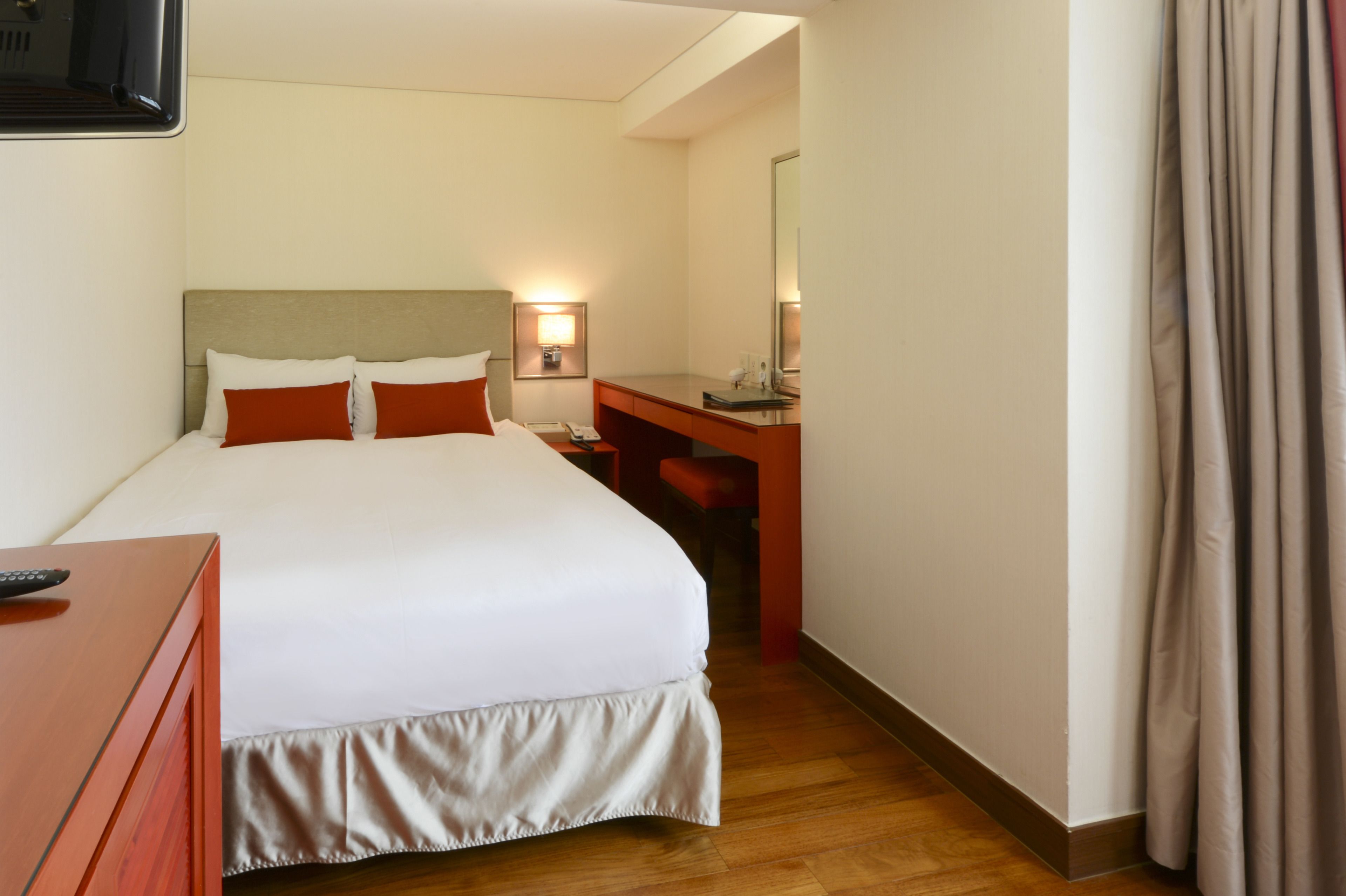 A hotel room with a bed, a desk, a chair, a mirror, and a TV.
