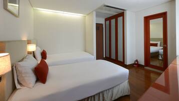 A hotel room with two beds, a bedside lamp, a fire extinguisher, and a mirror on the door.