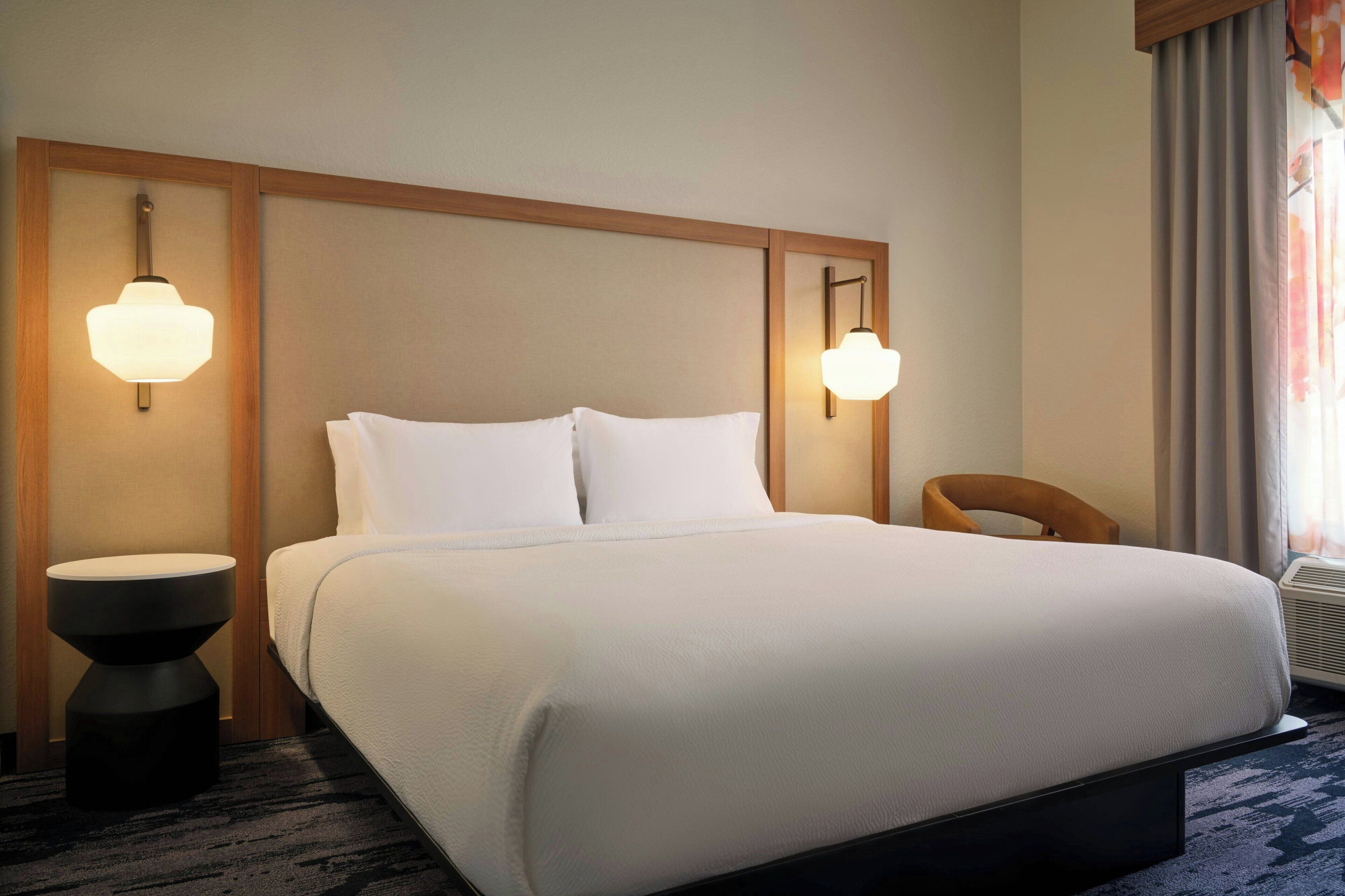 Una habitación de hotel con una cama grande, dos lámparas fijadas a la pared, una mesita redonda y una silla.