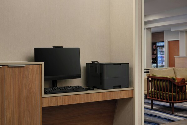 Habitación de hotel con un escritorio de madera, una computadora e impresora. Se ve un sofá y una cuna al fondo.