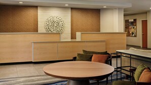 A hotel lobby with a round table, cushioned seating, a decorative wall, and a door in the background.