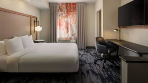 A hotel room with a bed, desk, chair, TV, and a window with curtains.