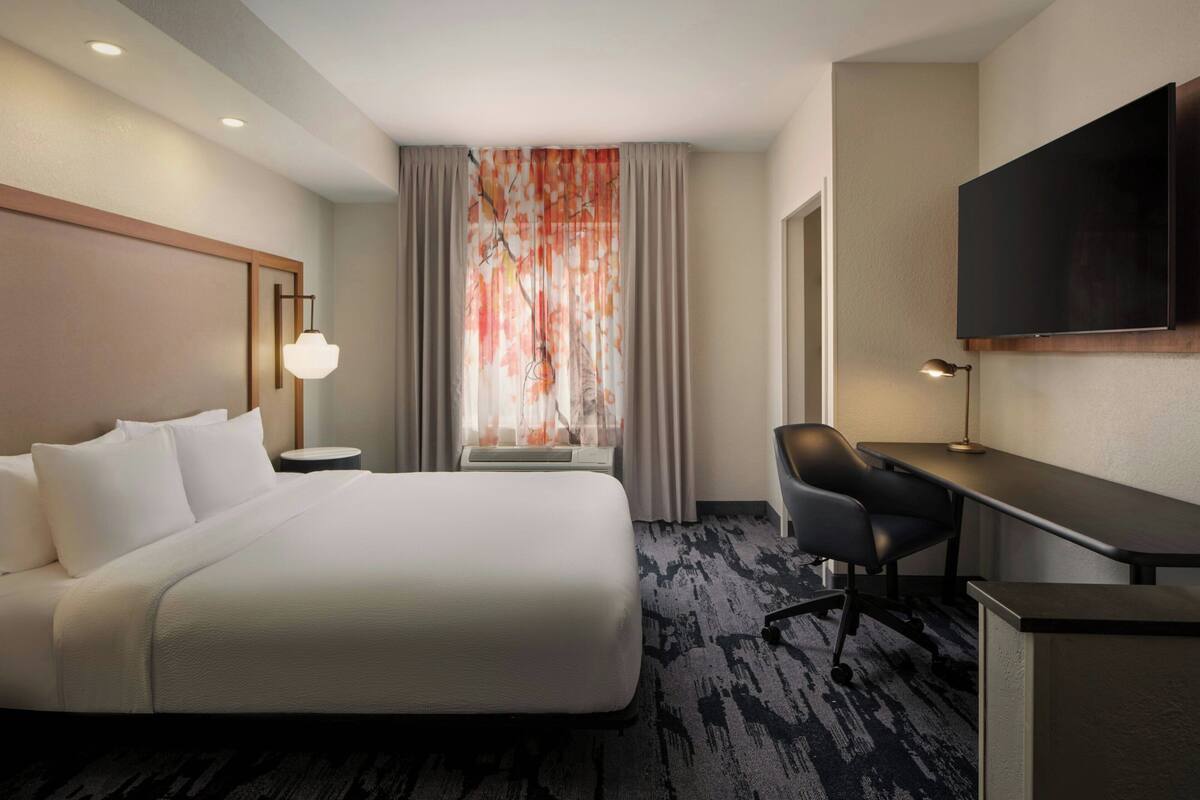 A hotel room with a bed, desk, chair, TV, and a window with curtains.